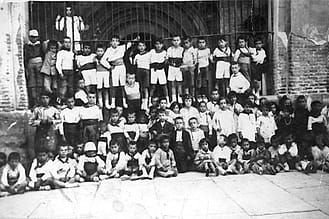 Década de 1920. En el centro, de pie y con camisa oscura y brazos en jarra, Paco Foti, con niños y niñas de su edad en el pórtico de la iglesia de San Juan.